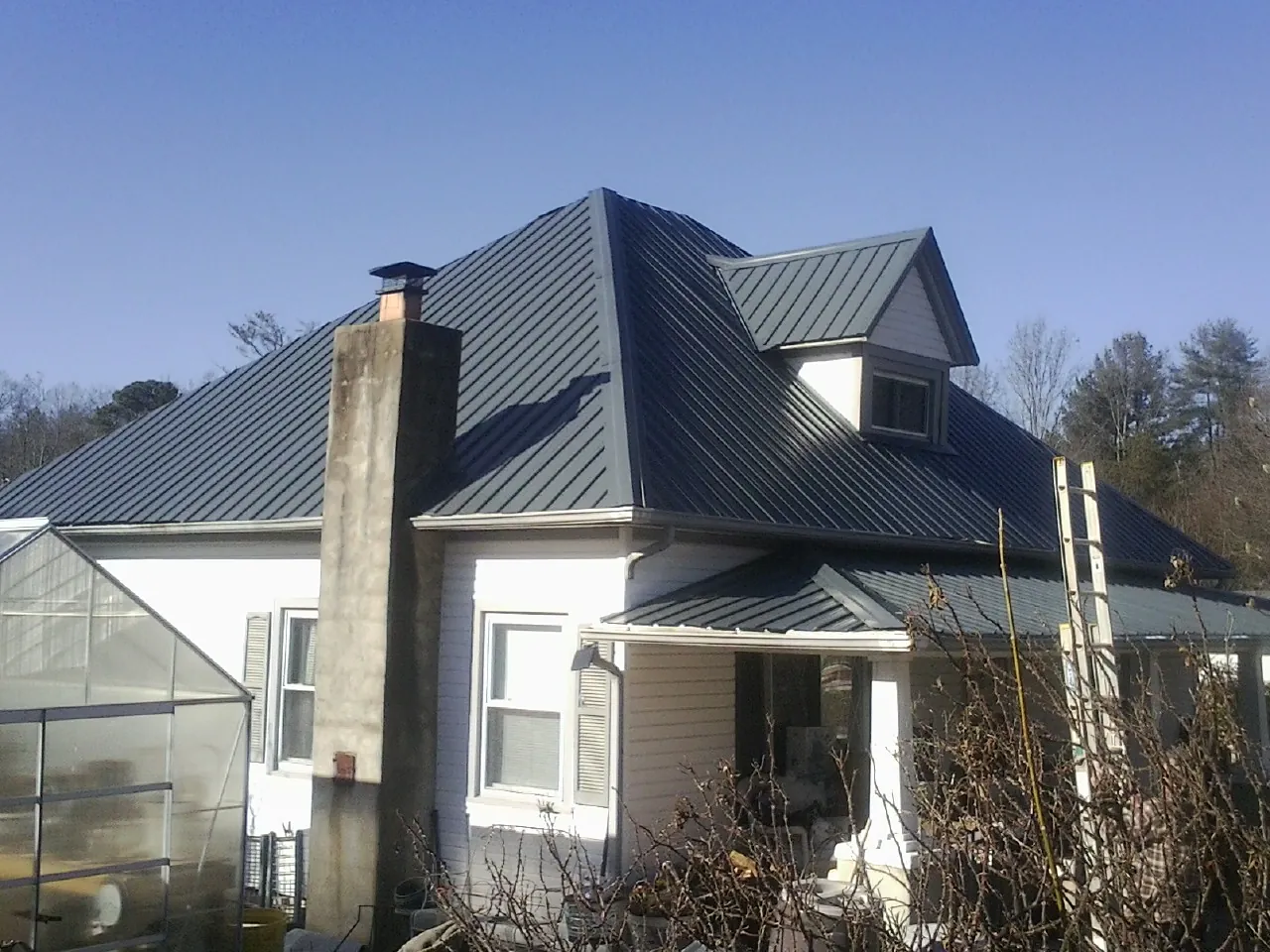 Dark blue standing seam metal roof on a white farmhouse with dormer — Slate & Tile Roof Repair by Roofing Brothers in East Stone Gap