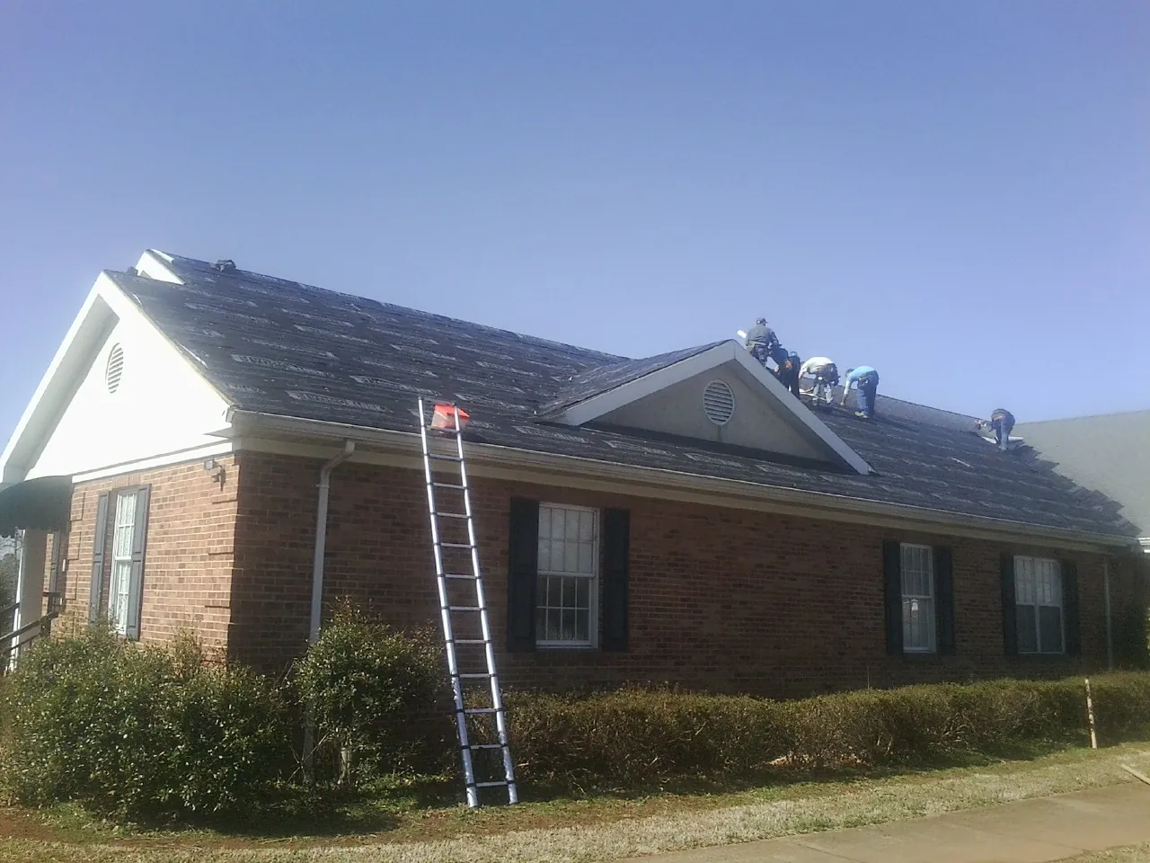 Crew tearing shingles off a brick ranch roof with a ladder set — Metal Roof Repair work by our crew in East Stone Gap