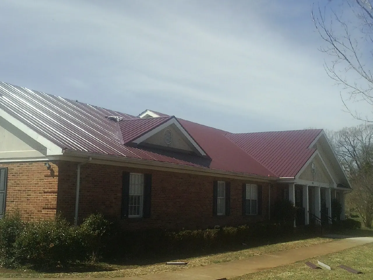 Red metal roof with gabled entries on a long brick building, from a Hail Damage Roof Repair job in East Stone Gap