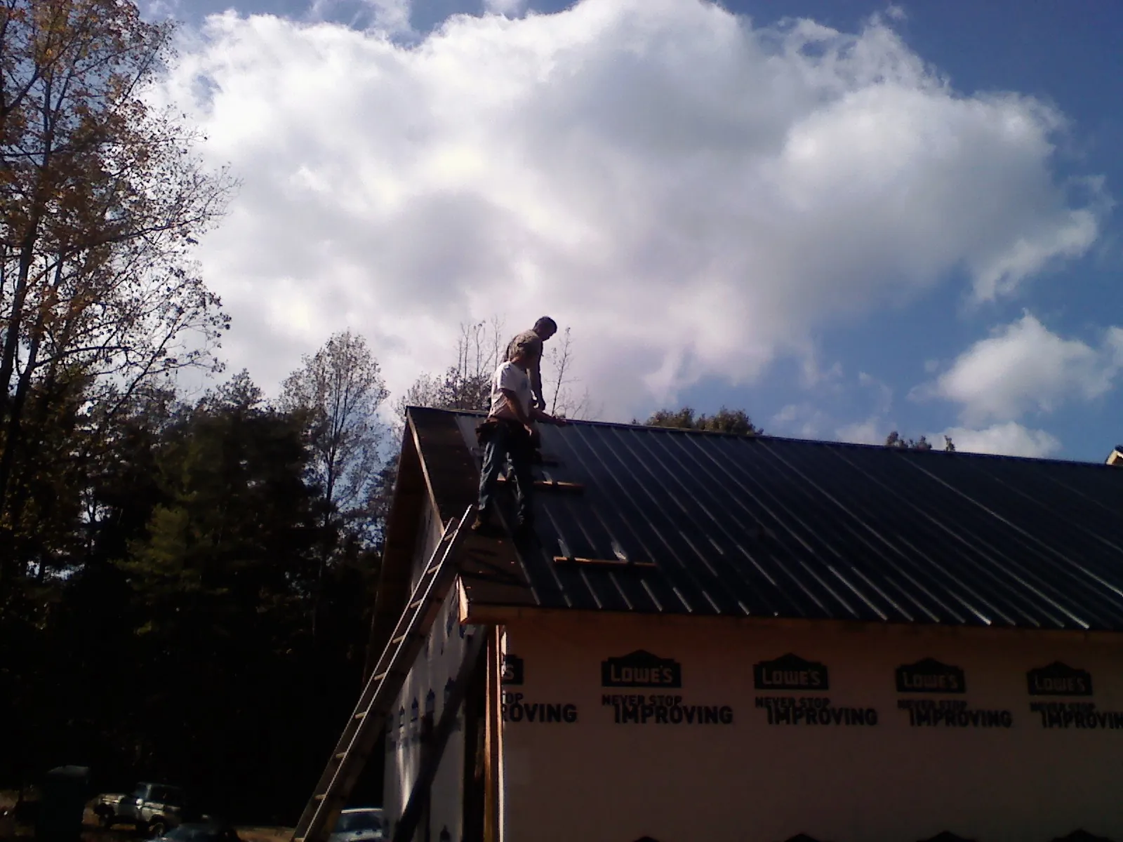 Roofer fastening dark metal panels high against a cloudy sky, from a Roof Inspection job in East Stone Gap
