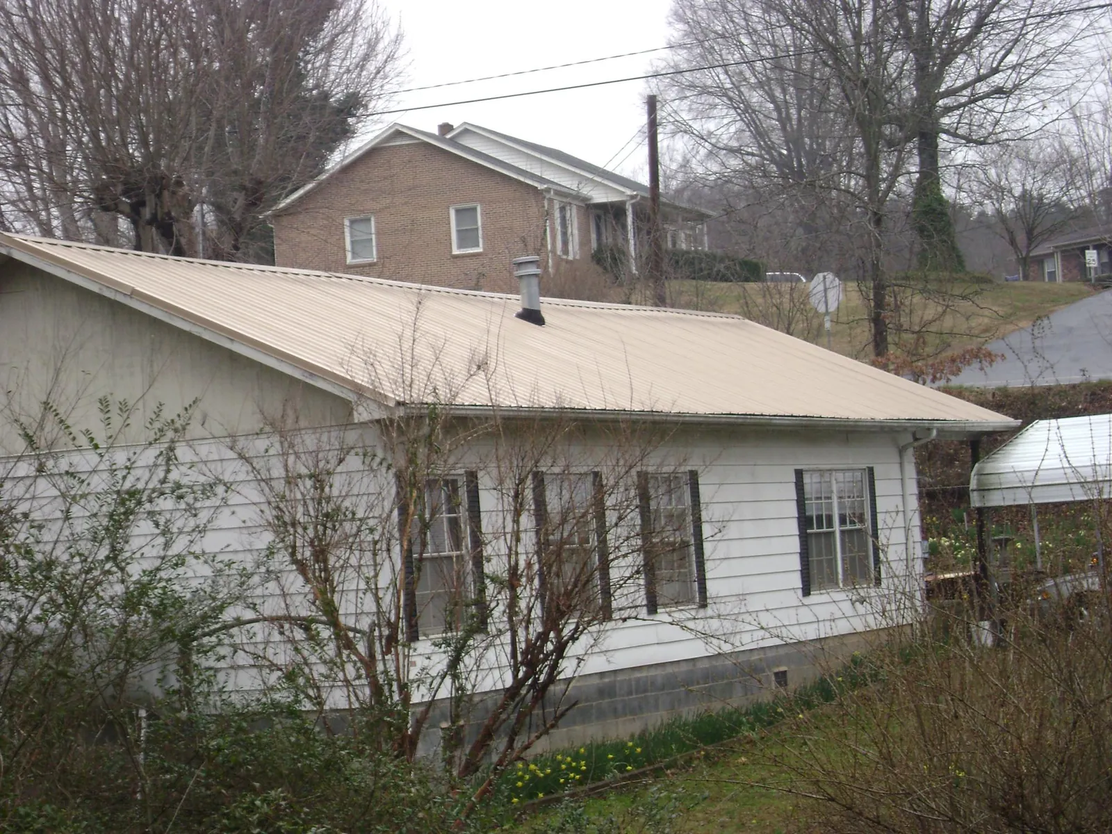 Tan metal roof on a white sided house set into a hillside — Commercial Roofing by Roofing Brothers in East Stone Gap